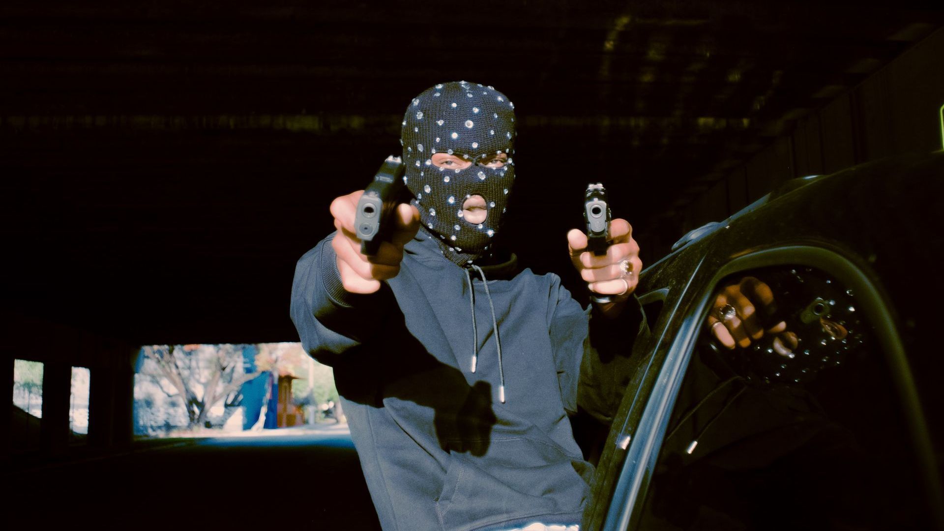 person wearing a mask pointing two guns.
