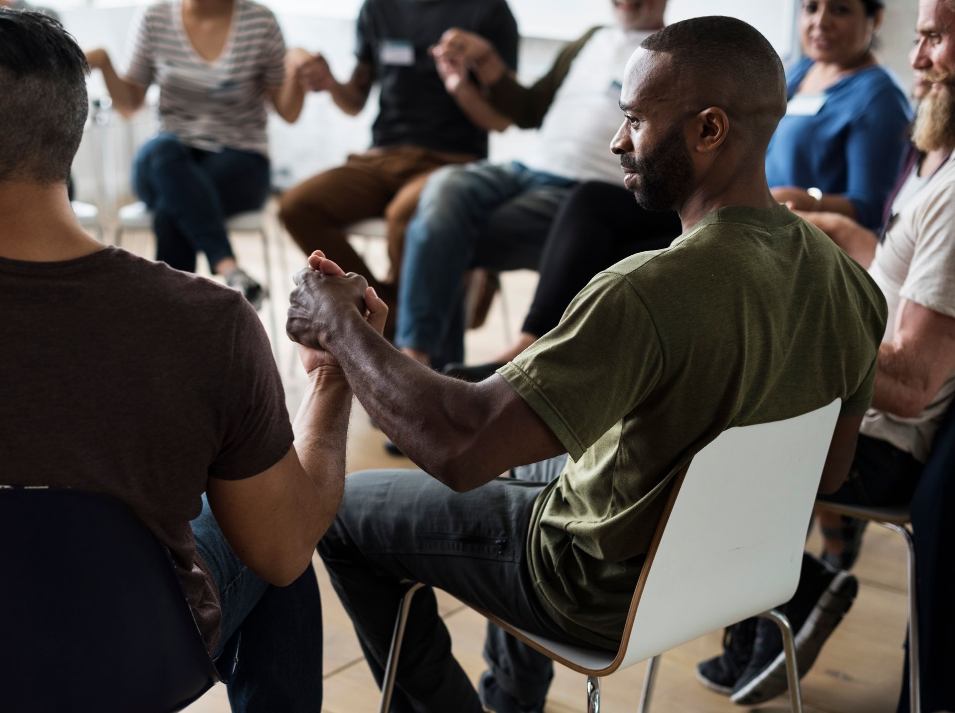 Group of people in a circle holding hands, likely a support or therapy session. Focus on a Black man.