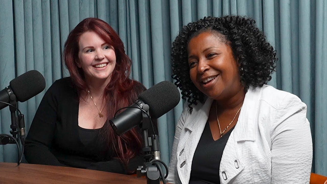 Two women are sitting at a table in front of microphones.