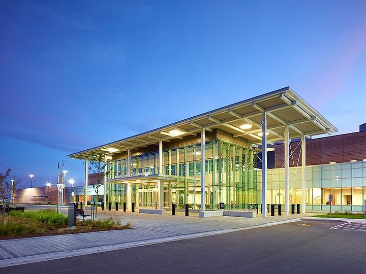 Modern building entrance with glass walls, under a metal overhang, dusk.