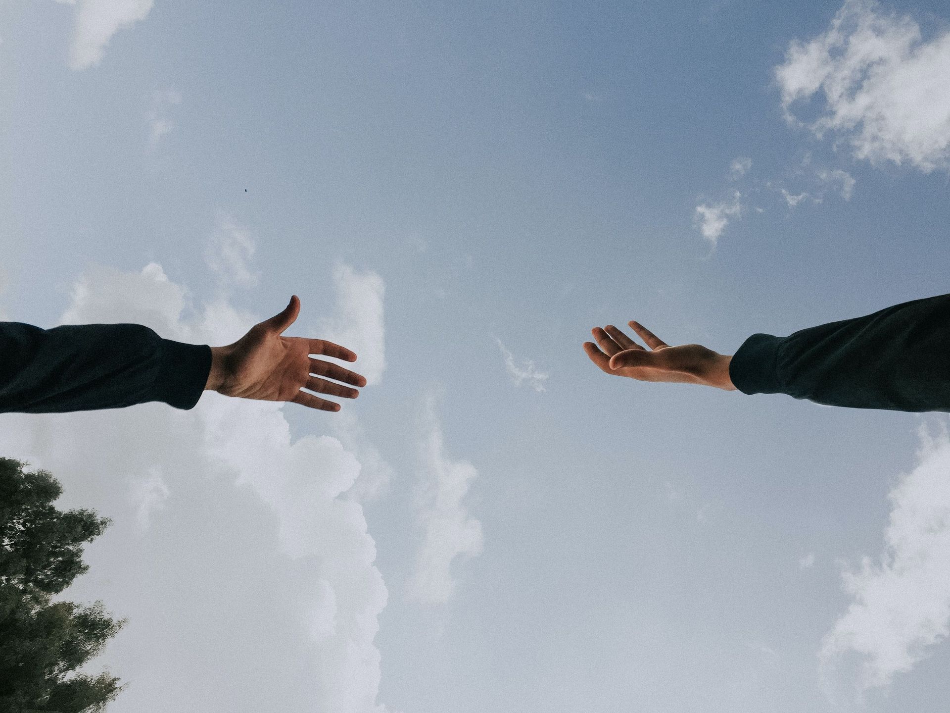 two hands reaching out towards each other against a cloudy sky