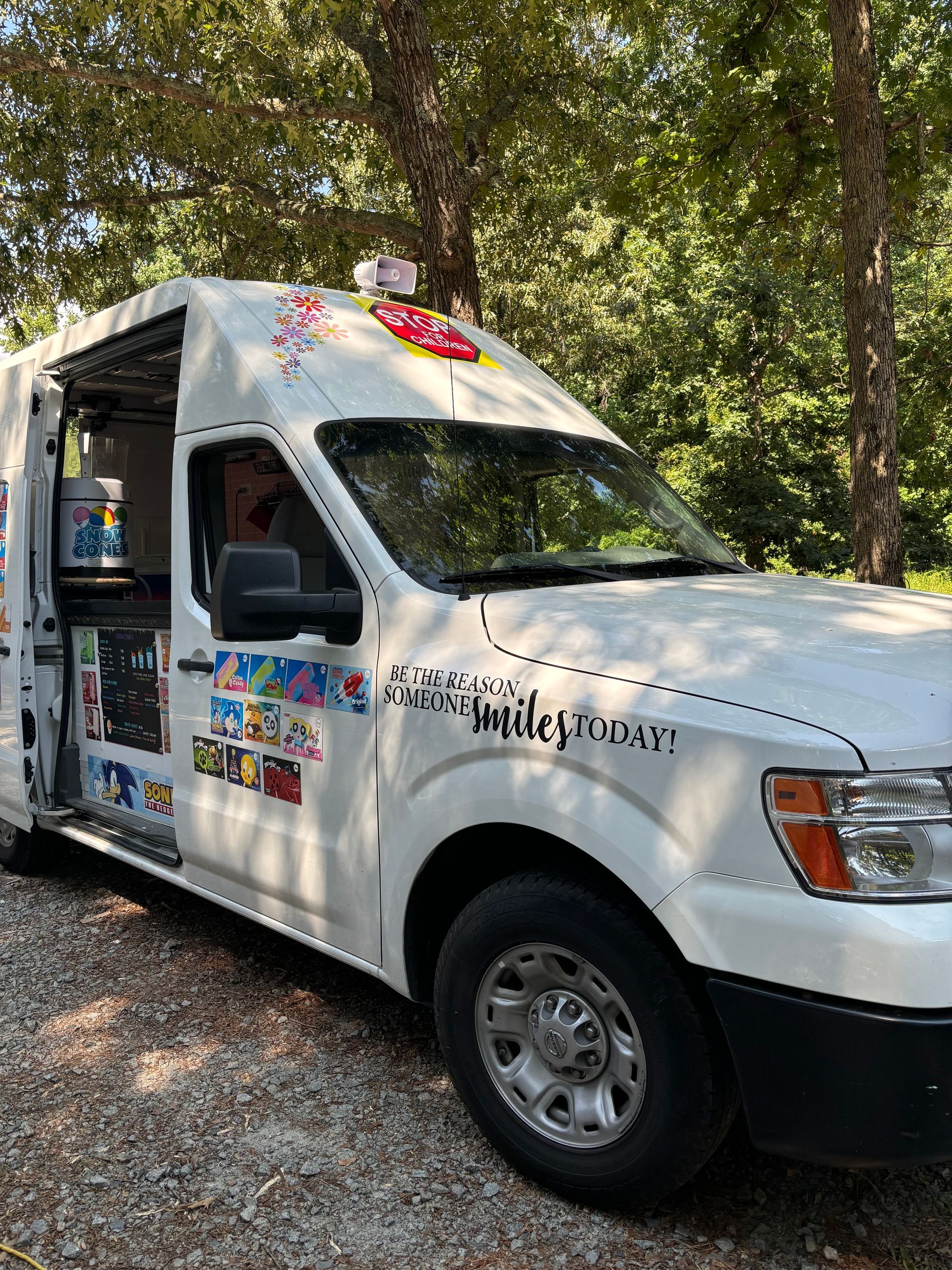 A white ice cream truck is parked in the woods.