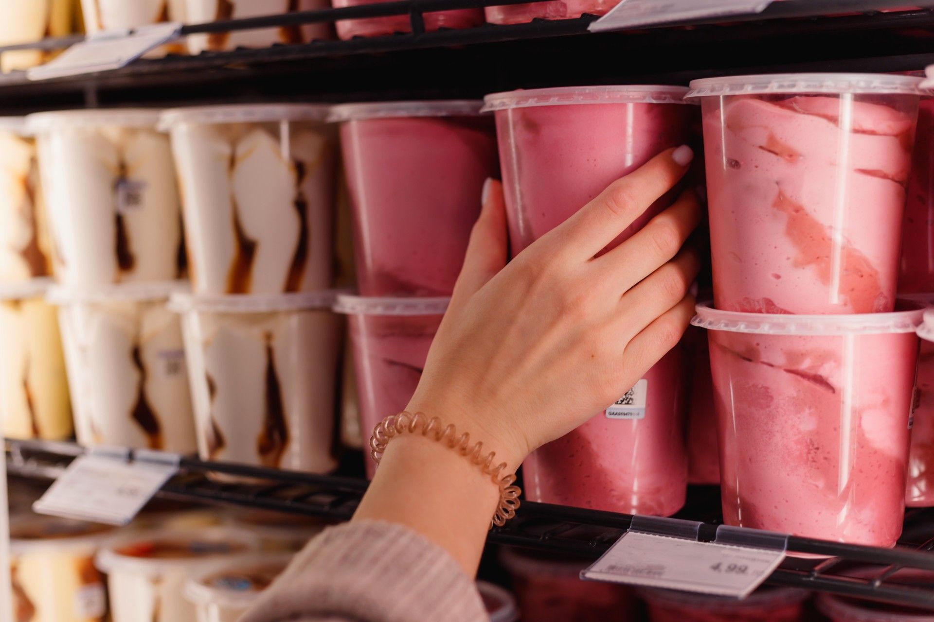 A woman is reaching for a cup of ice cream in a refrigerator.