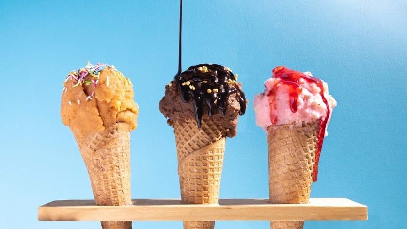 Three ice cream cones are sitting on a wooden shelf.