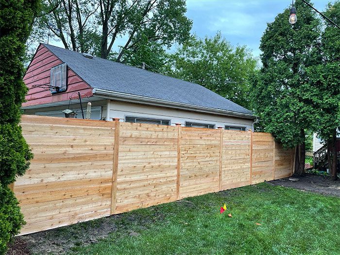 A wooden fence with a green trash can in front of it.