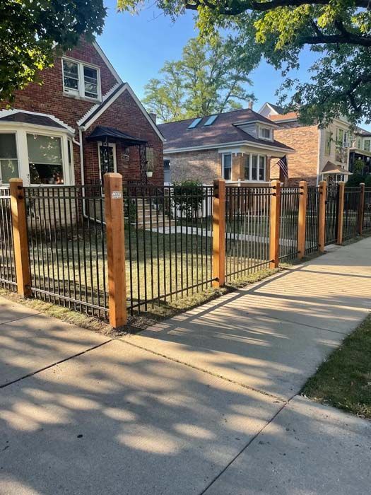 A wooden fence along a sidewalk in front of a brick house.
