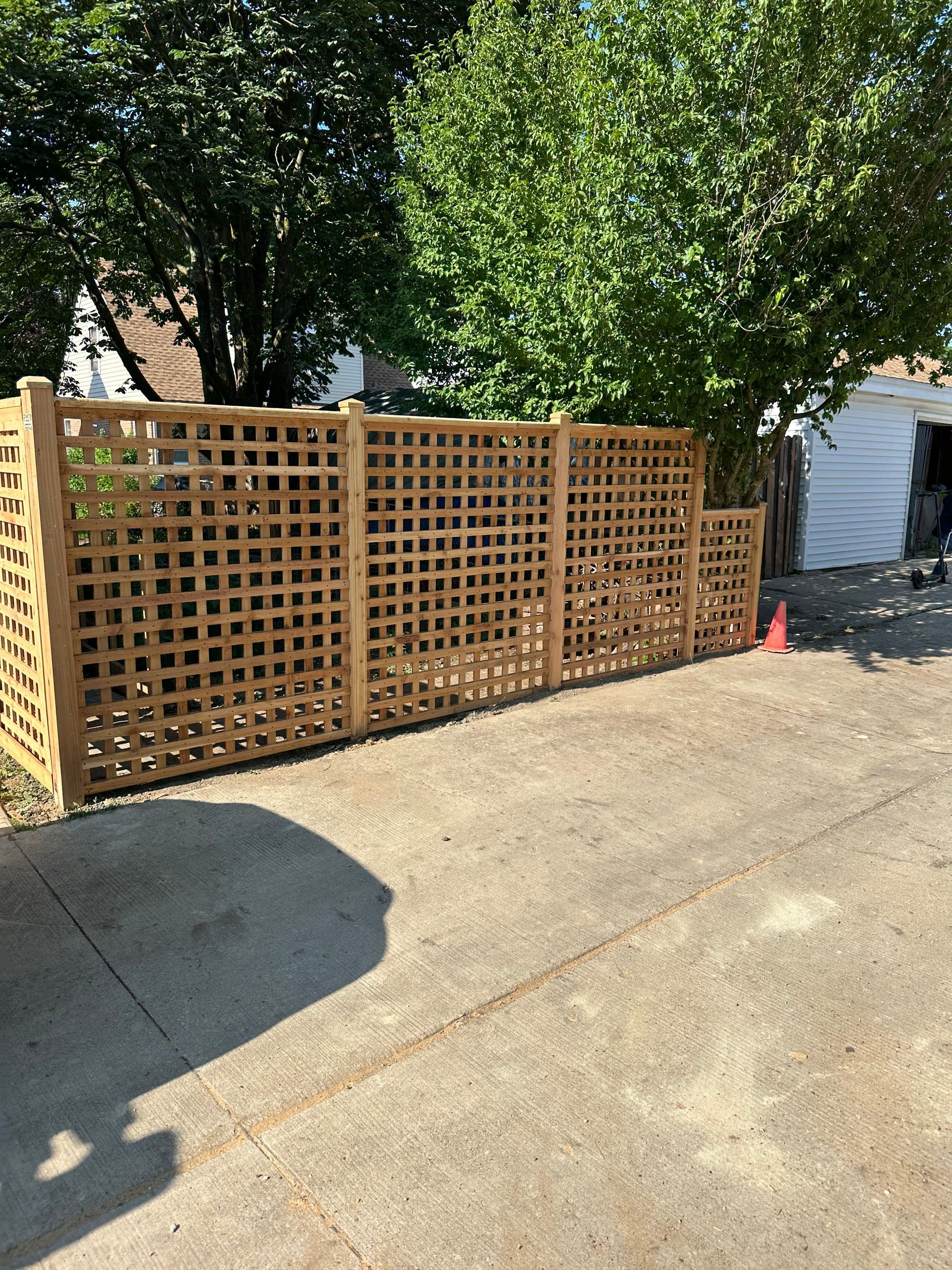 A wooden fence is sitting on the side of a driveway next to a garage.
