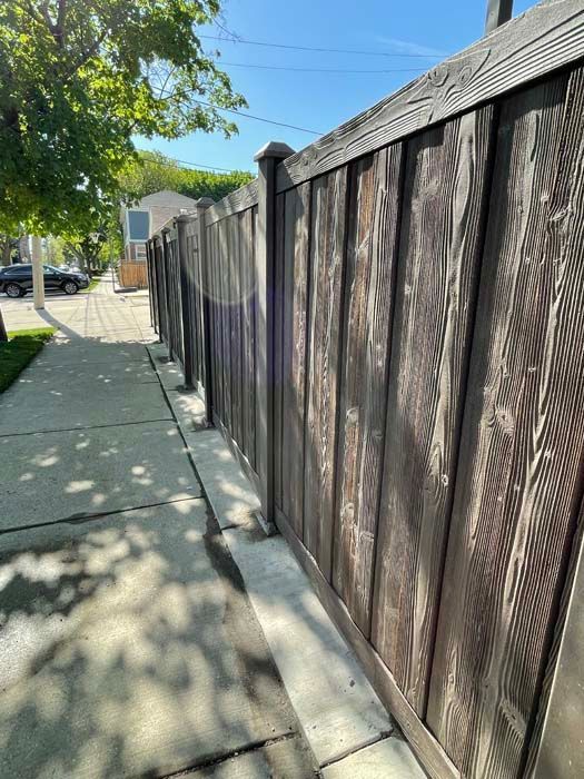 A wooden fence along a sidewalk next to a house.