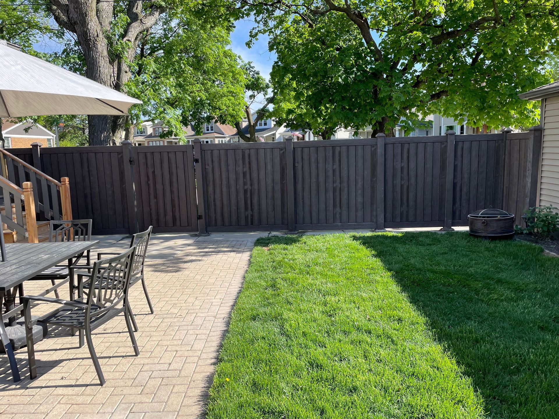 A wooden fence surrounds a patio with a table and chairs.