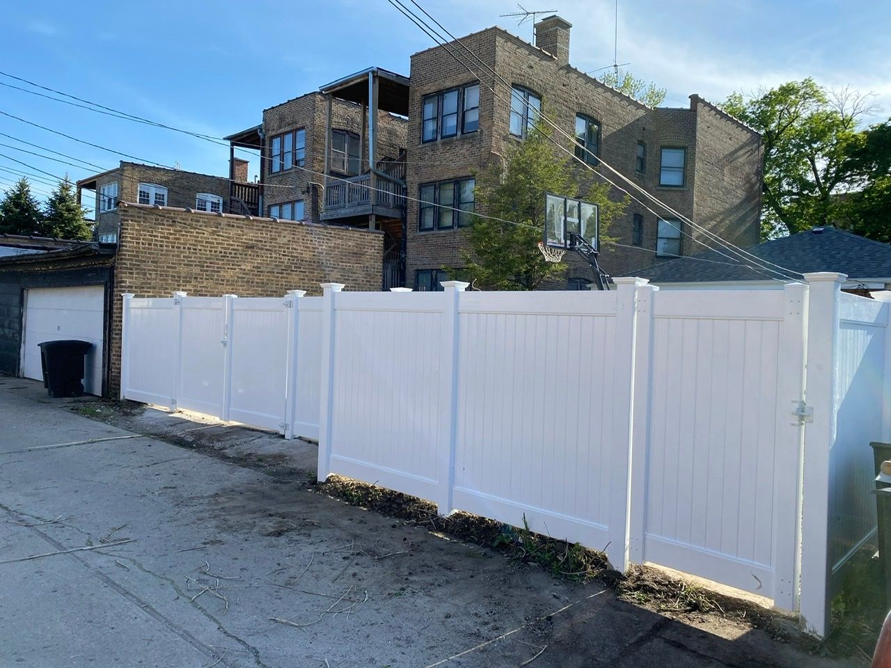 A white fence is in front of a brick building.