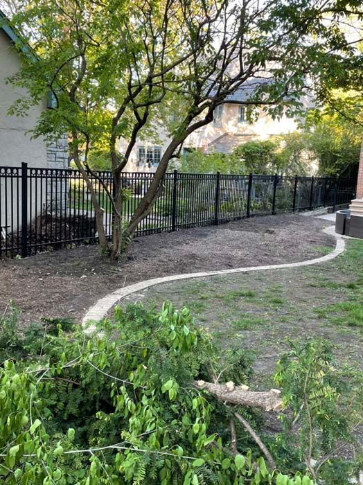 A black fence surrounds a yard with a path leading to a house.