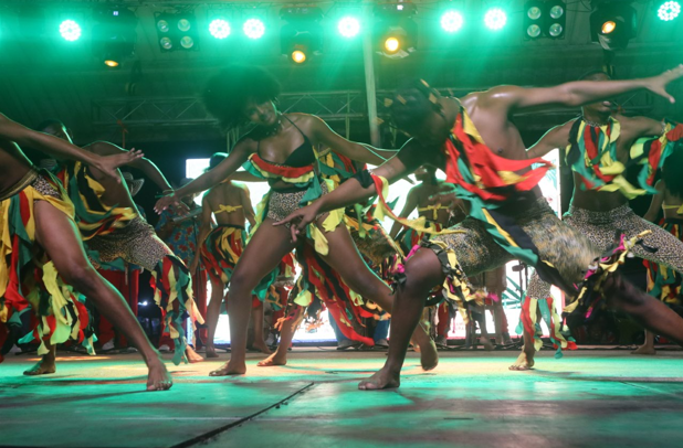 Bailarines en el escenario, actuando con trajes coloridos bajo luces verdes del escenario.