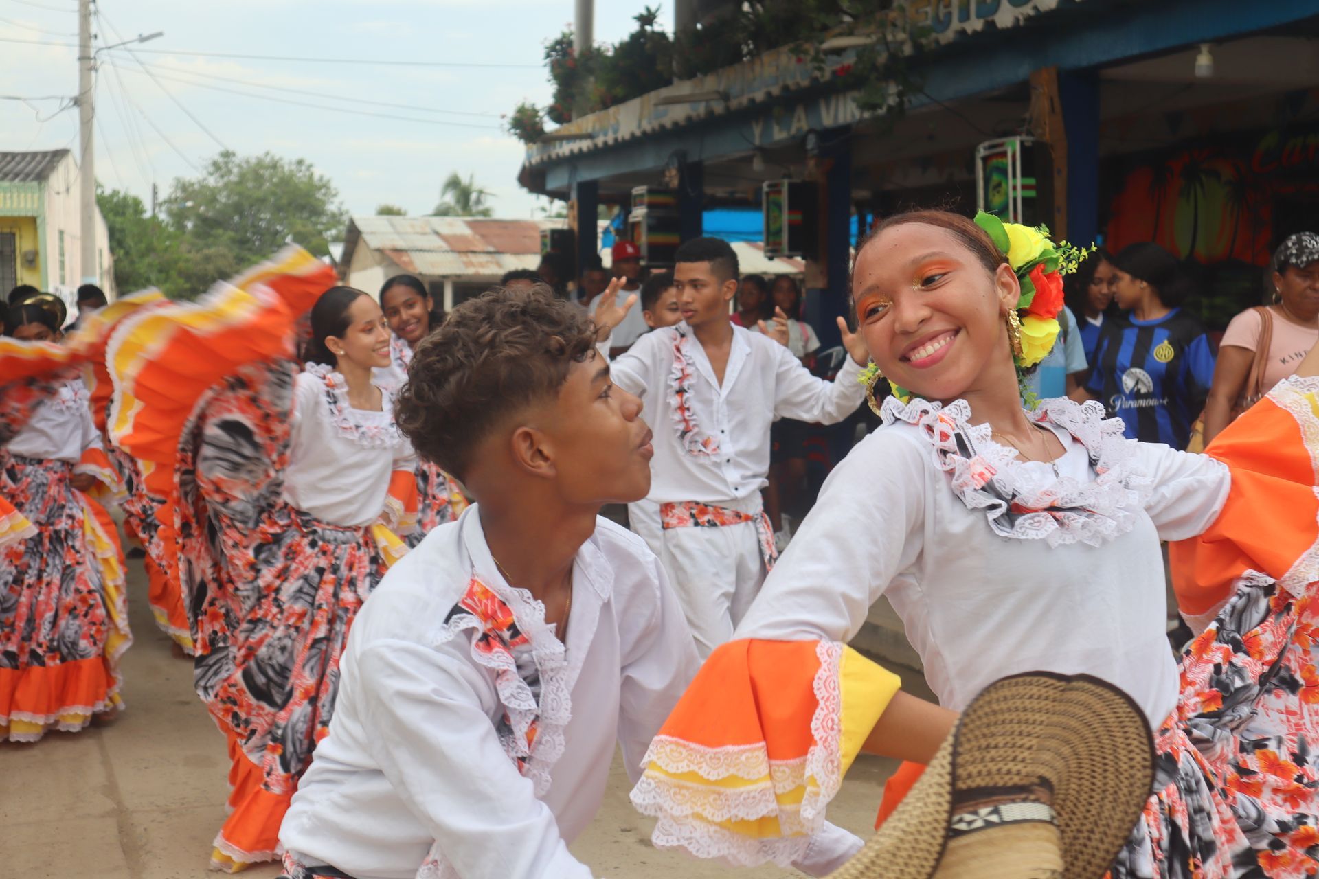Gente bailando en la calle. Una mujer sonríe a la cámara. Vestidos coloridos, atuendos festivos.