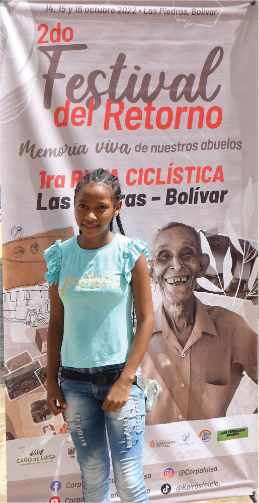 Una niña está parada frente a una pancarta que dice festival del retorno