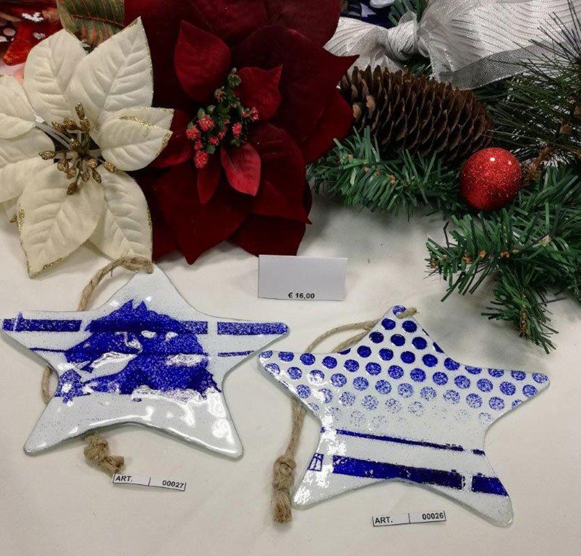 Due decorazioni a forma di stella con motivi blu e spago sono appese vicino alle decorazioni natalizie: stelle di Natale bianche e rosse, pigna.