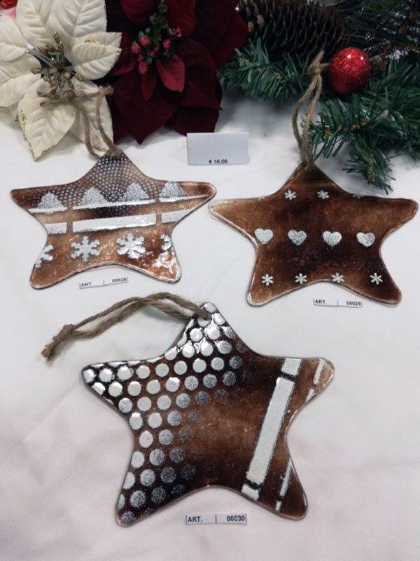 Tre decorazioni natalizie a forma di stella marroni e argentate con vari motivi, appese con uno spago, esposte vicino alle decorazioni festive.