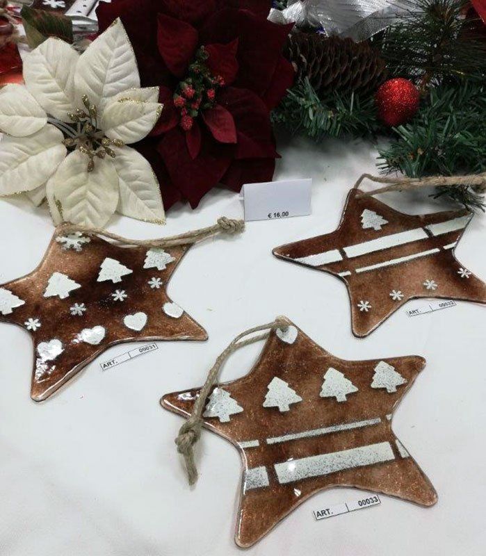 Tre decorazioni natalizie marroni a forma di stella con disegni bianchi e anelli di spago per appenderle; stelle di Natale sullo sfondo.