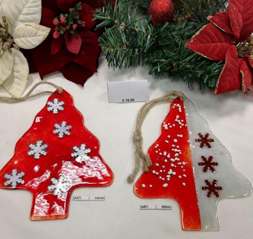 Due decorazioni natalizie in vetro, rosse e bianche con dettagli a forma di fiocco di neve, su una superficie bianca, con decorazioni natalizie.