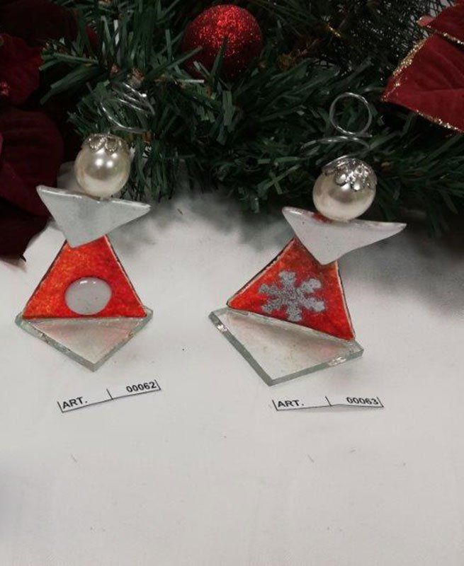 Due ornamenti natalizi in vetro colorato a forma di angelo: corpo rosso, ali bianche, teste di perle, ganci d'argento, appoggiati su una superficie bianca.