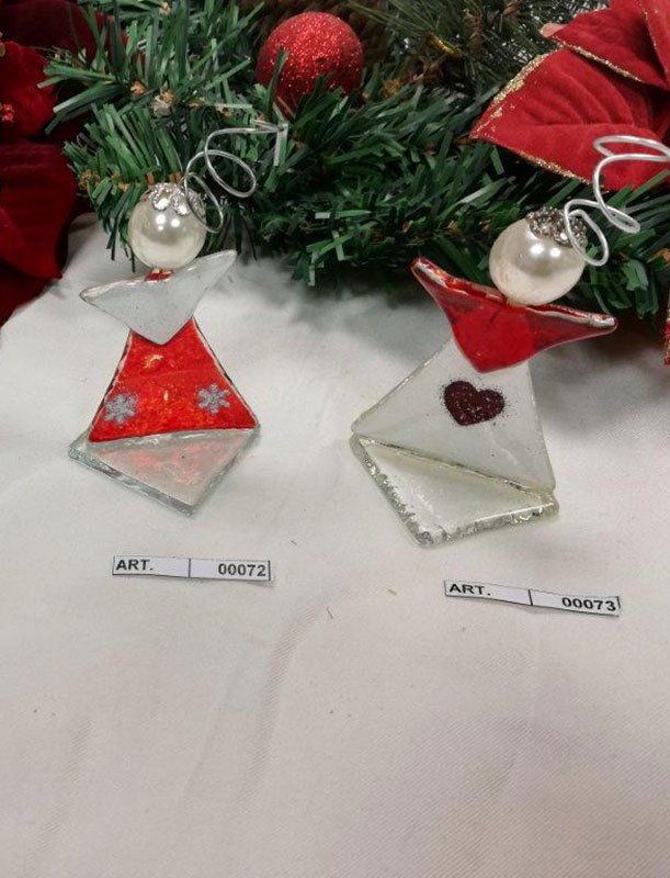 Due ornamenti natalizi a forma di angelo fatti a mano su superficie bianca. Uno rosso, uno bianco, con teste di perle.