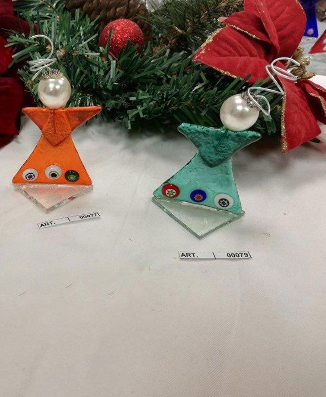 Due ornamenti in vetro a forma di angelo davanti a una ghirlanda natalizia; arancione e verde acqua con fondi in vetro decorativi.