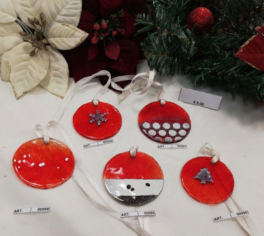 Cinque decorazioni natalizie rosse, fatte a mano e rotonde, con nastri bianchi, esposte su una superficie bianca con decorazioni stagionali.