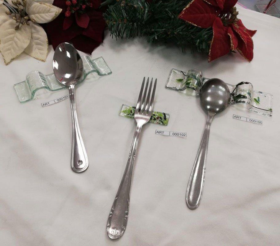 Tre posate d'argento (cucchiaio, forchetta, cucchiaino) su una tovaglia bianca, ciascuna fissata con un nastro decorativo verde e bianco.