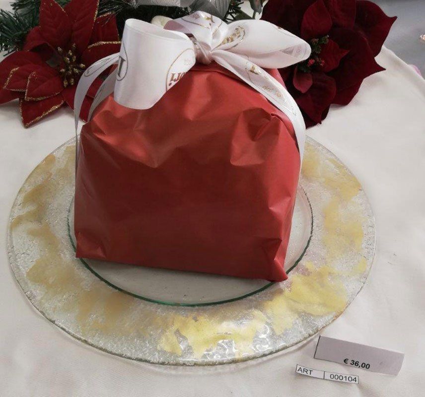 Un regalo incartato di rosso, legato con un fiocco su un piatto con bordo dorato, con un'etichetta con il prezzo.