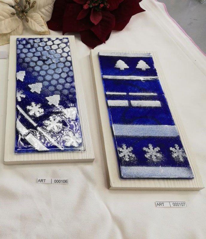 Due opere d'arte in vetro fuso blu e bianco con motivi invernali, montate su basi di legno.