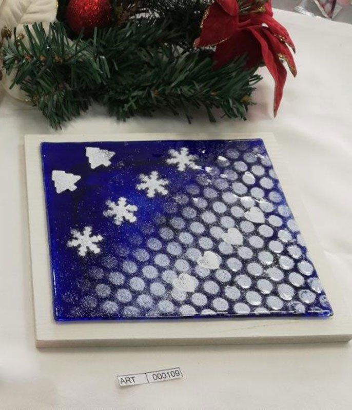 Opera natalizia in vetro blu con fiocchi di neve bianchi e sagome di alberi.