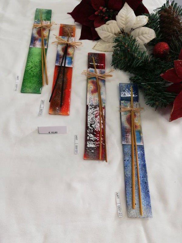 Quattro porta incenso in vetro colorato, ciascuno con un bastoncino, legati con spago, vicino alle decorazioni natalizie.
