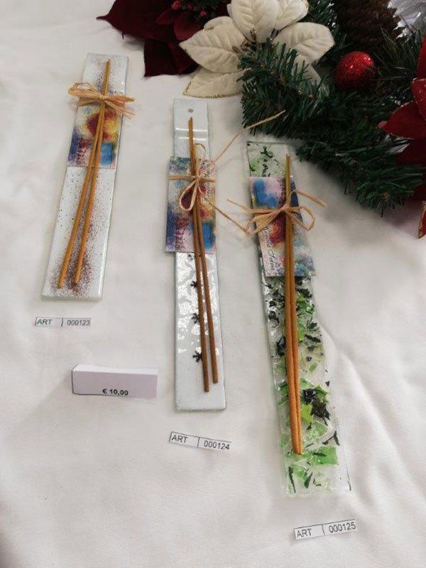 Tre bacchette di vetro, con le bacchette legate, sono appoggiate su una superficie bianca, vicino alle decorazioni natalizie.