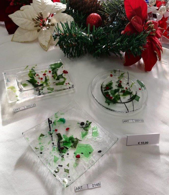 Piatti in vetro fuso con accenti verdi e rossi, esposti con decorazioni natalizie su una tovaglia bianca.