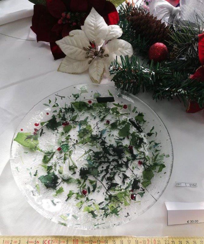Piatto trasparente con foglie verdi schiacciate e bacche rosse; sfondo con decorazioni festive.
