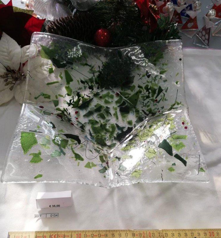 Ciotola in vetro trasparente con dettagli a foglia verde su una superficie bianca, con decorazioni natalizie sullo sfondo.