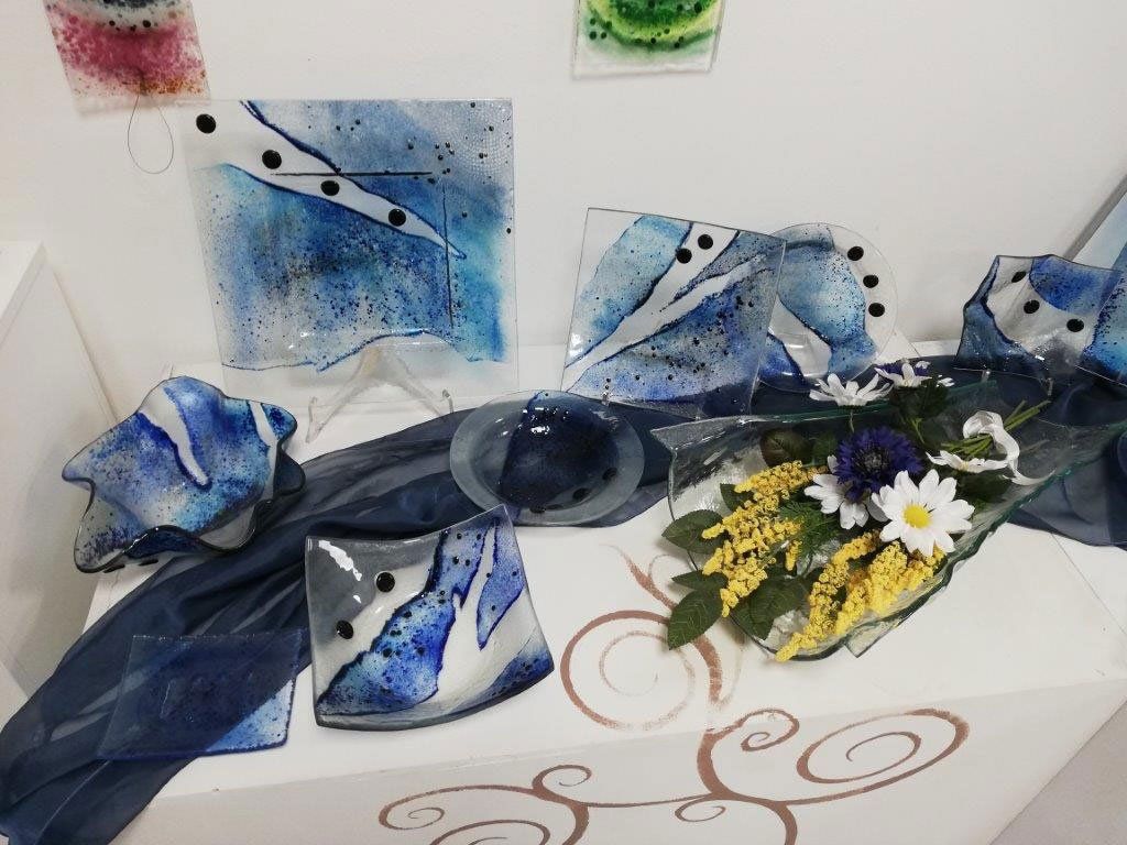 Esposizione di opere d'arte in vetro blu e fiori su una superficie bianca.