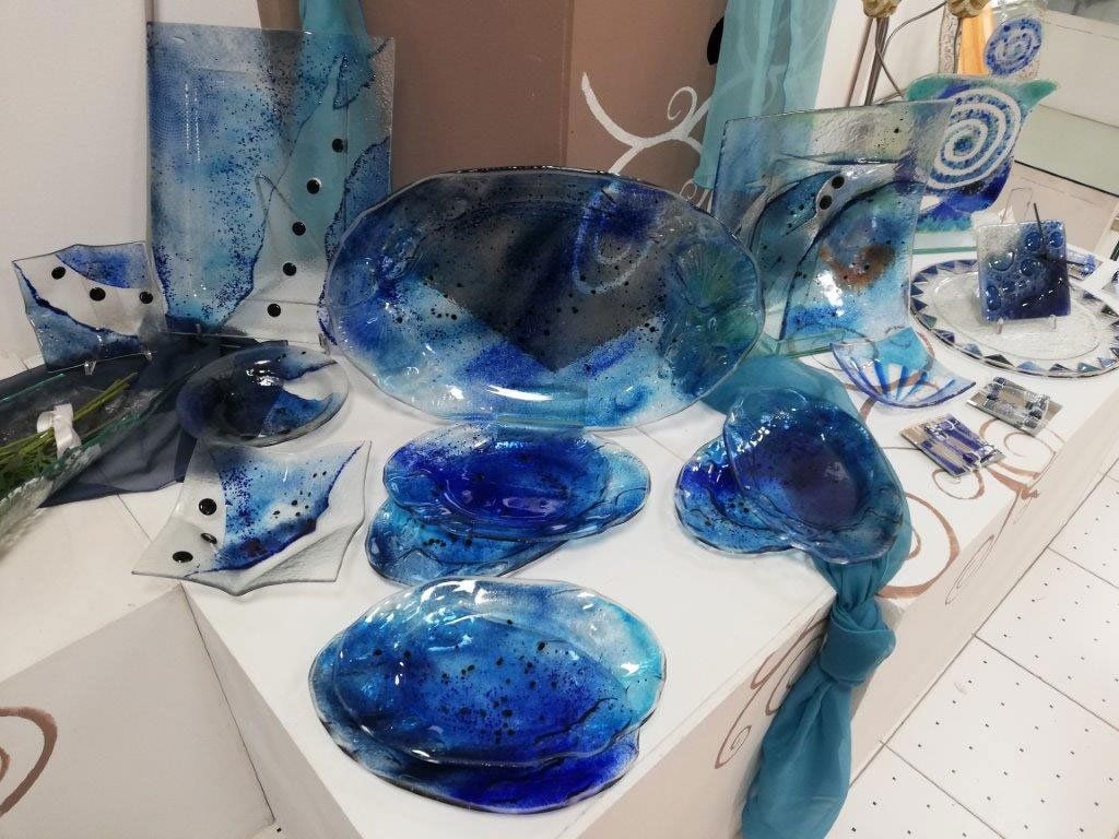 Bicchieri nei toni del blu, esposti su un tavolo bianco. Include piatti, ciotole e un vaso.