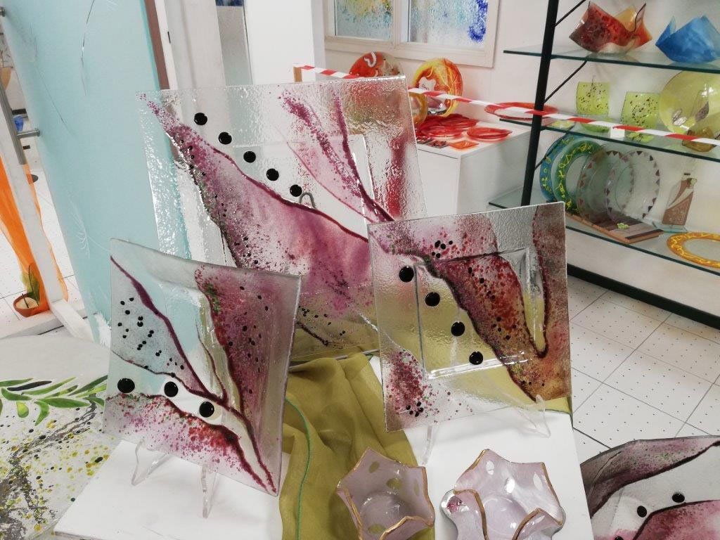 Esposizione di opere d'arte in vetro con colorati disegni astratti; interno del negozio.