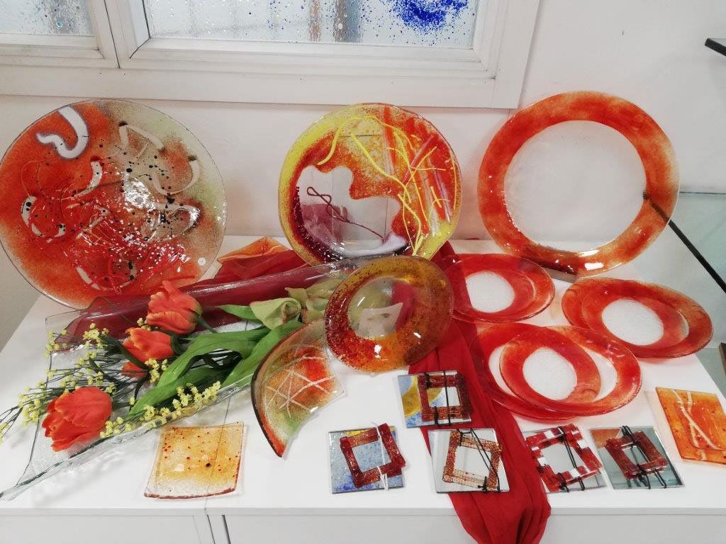 Piatti di vetro e pezzi decorativi nelle tonalità dell'arancione e del rosso esposti su una superficie bianca.