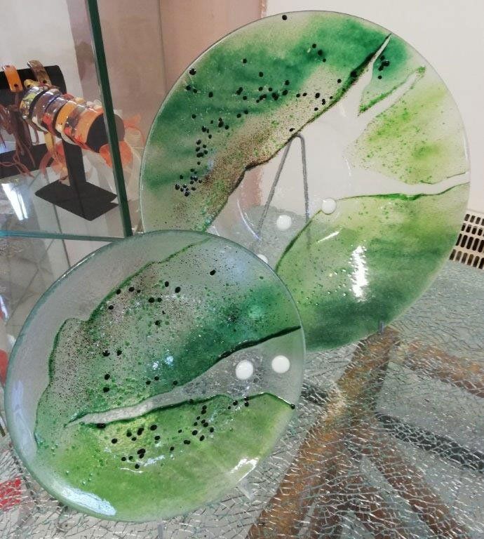 Due piatti di vetro con disegni astratti verdi e bianchi, esposti su un tavolo di vetro.