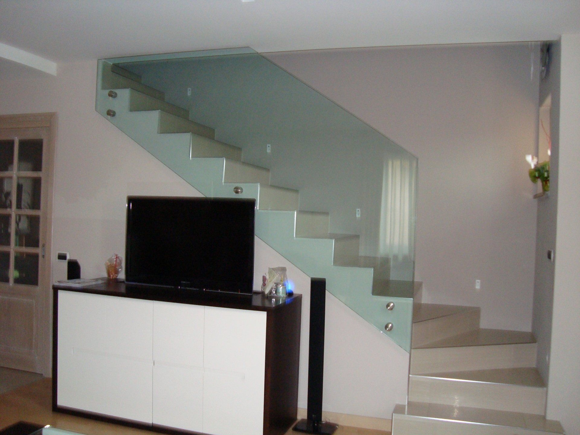 Scala sospesa in vetro con mobile bianco e marrone che ospita una TV.