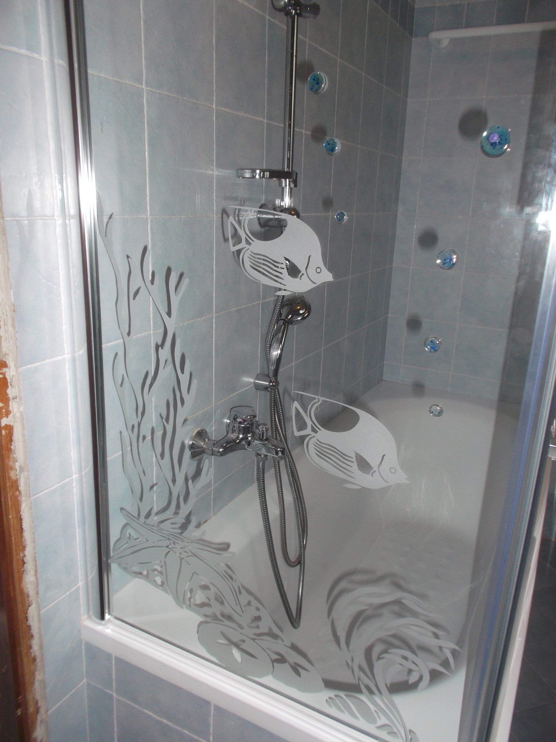 Box doccia con disegni di pesci e coralli incisi su una parete piastrellata di blu. Rubinetti doccia cromati all'interno.