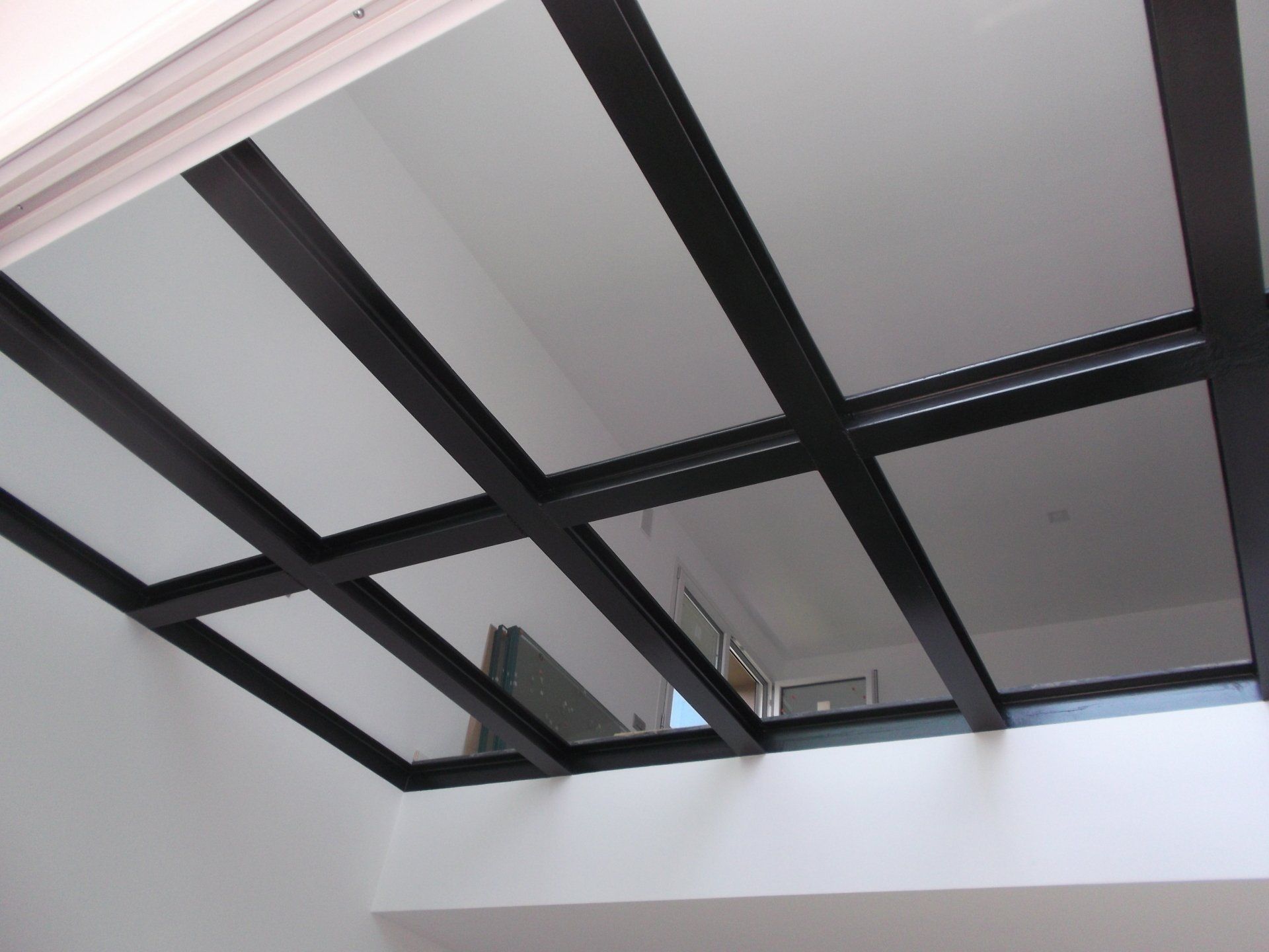 Lucernario con cornice nera e pannelli in vetro in una stanza con pareti bianche, visto dal basso.