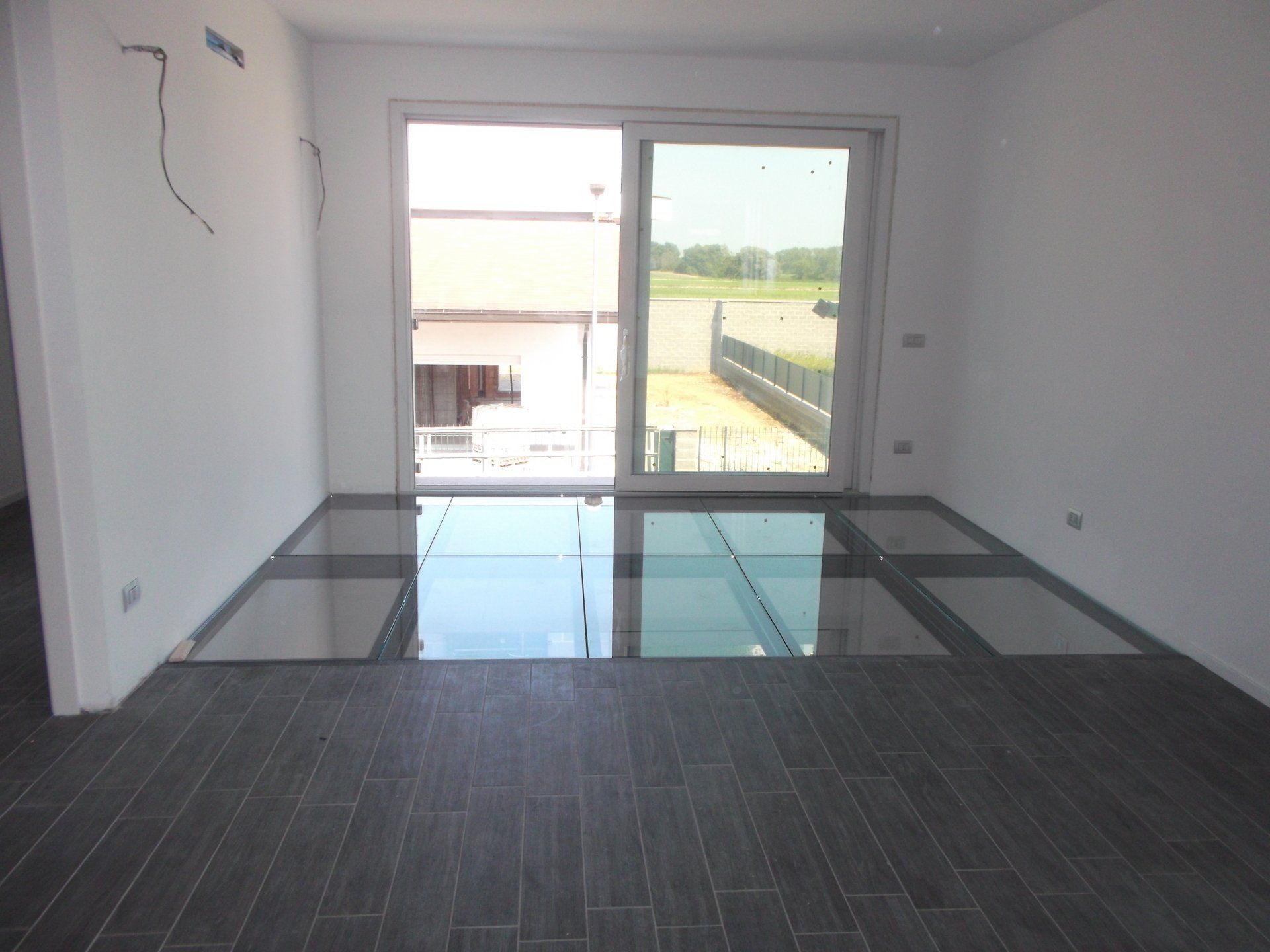 Stanza vuota con sezioni di pavimento in vetro e grande finestra con vista sull'esterno.