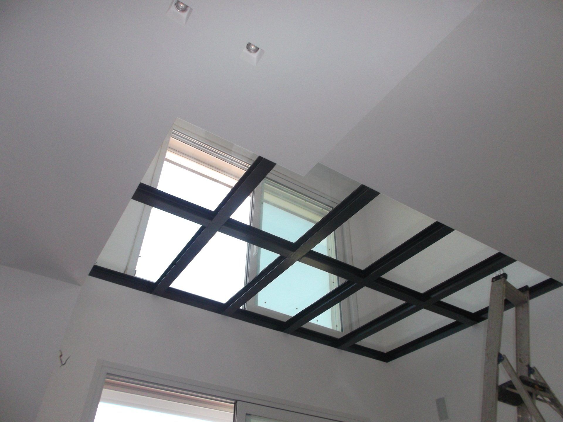 Soffitto con lucernario incorniciato da travi scure; pareti bianche, scala.