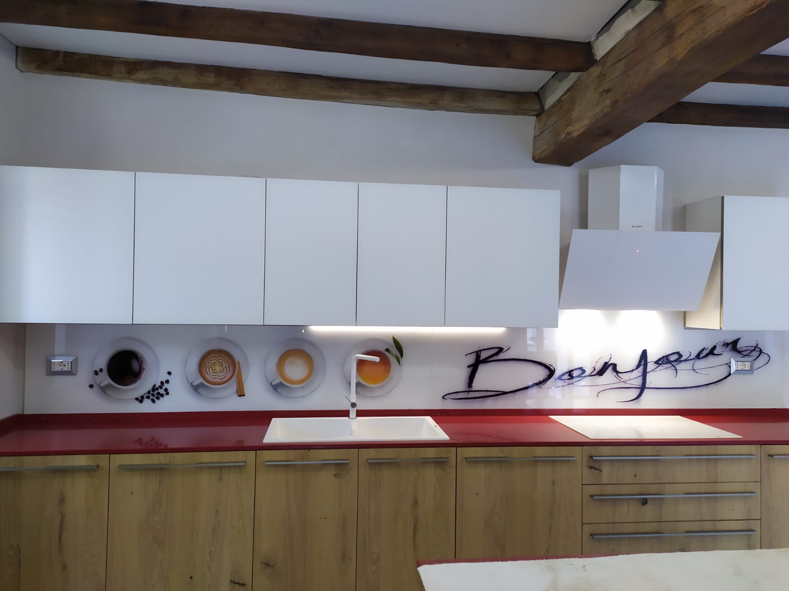 Cucina moderna con mobili bianchi, piano di lavoro rosso, mobili inferiori in legno e paraschizzi decorativo