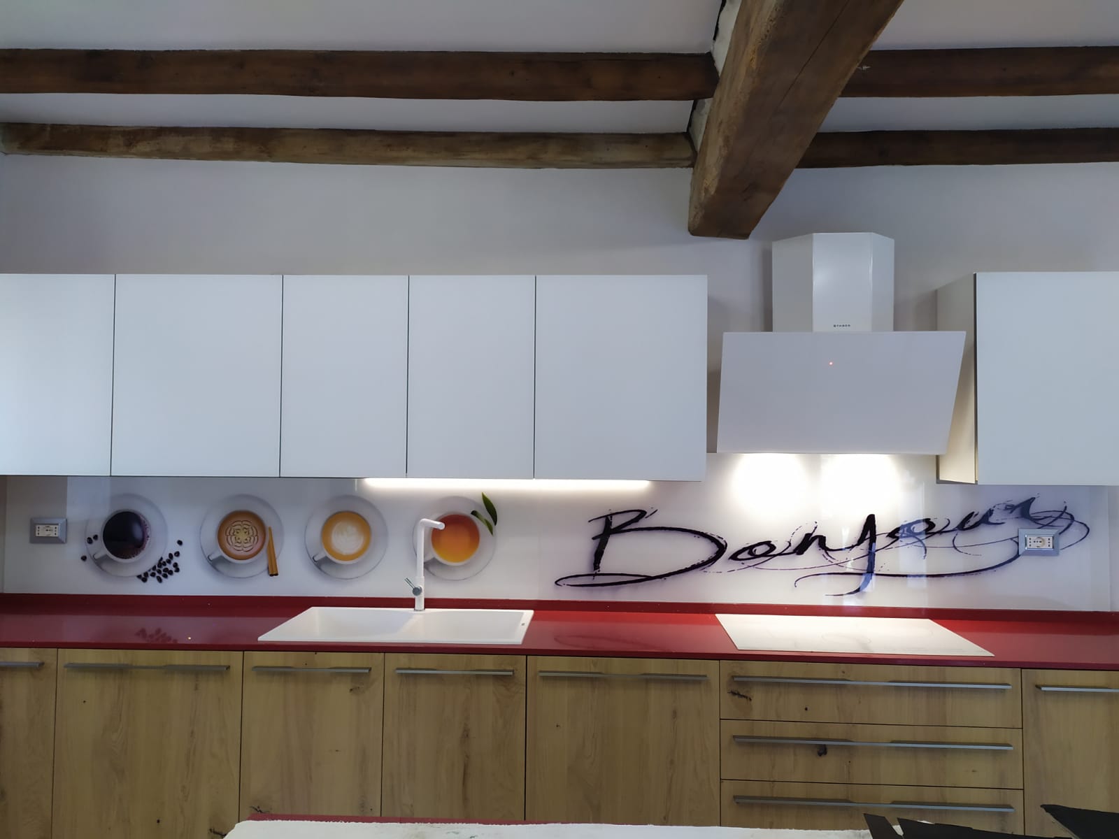 Cucina moderna con mobili bianchi, ripiani rossi e paraschizzi decorato con motivi di tazze da caffè e la scritta
