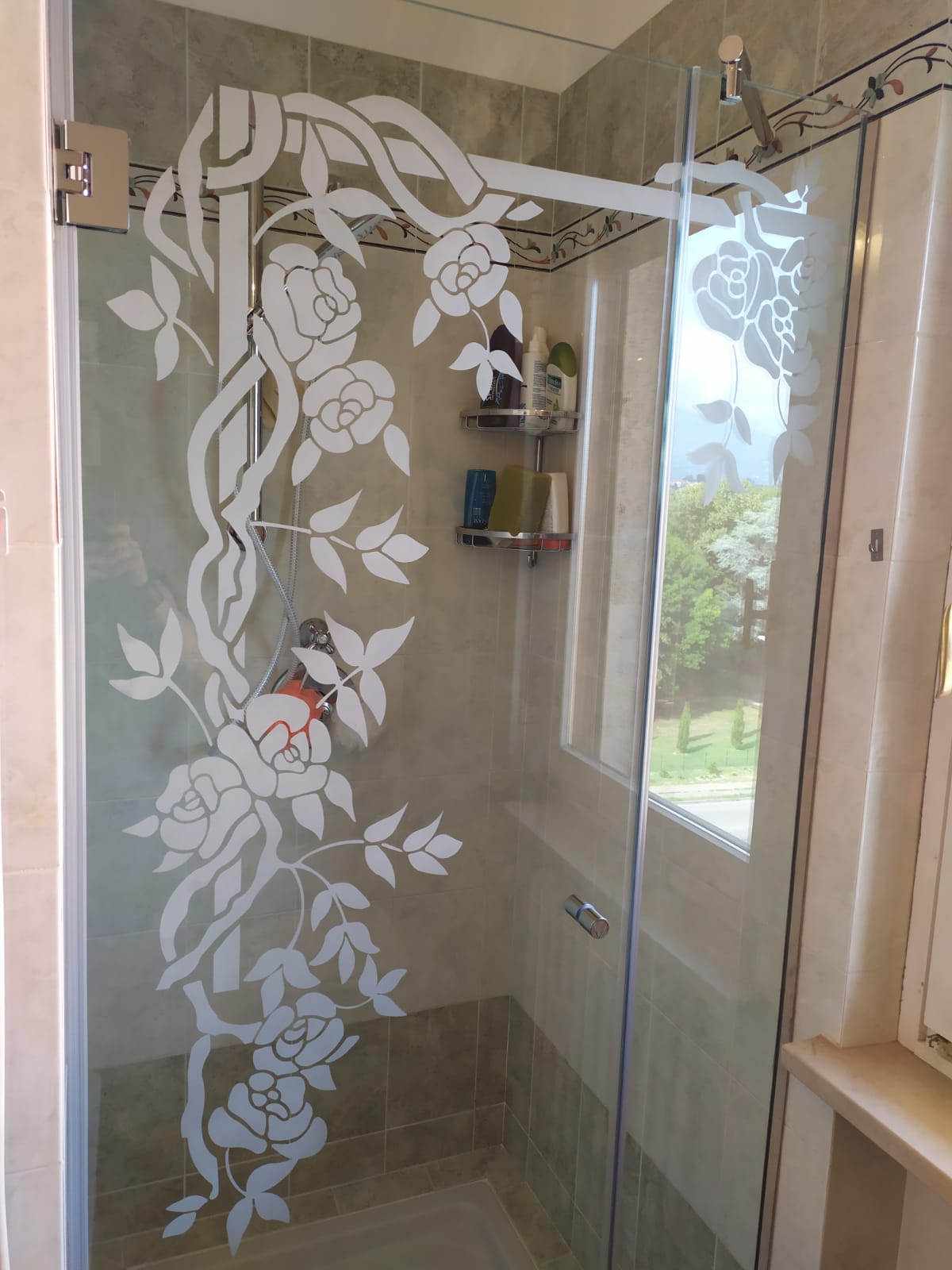 Doccia con motivo floreale satinato sulla porta in vetro, pareti piastrellate beige.