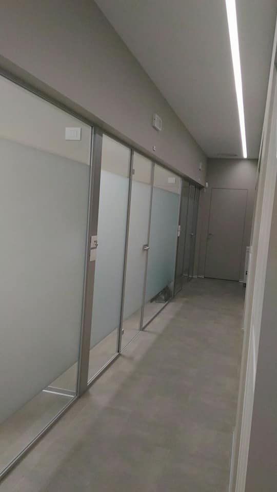 Corridoio con porte in vetro smerigliato, pareti grigie e un lampadario lineare.