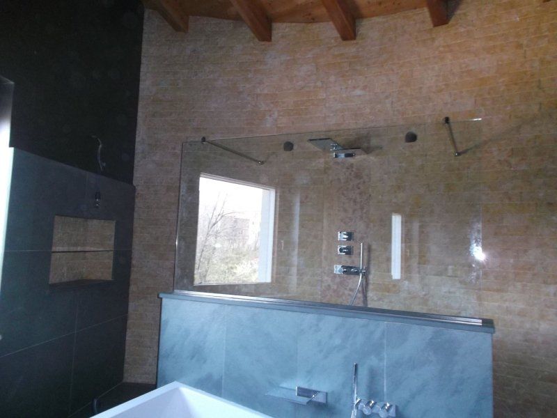 Bagno con box doccia in vetro, pareti grigie e una piccola finestra.